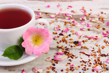 Cup of tea with wild rose flower on old rustic wooden background