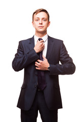 Stylish young man in suit and tie. Business style. Handsome man is standing, looking at the camera and fixing his tie