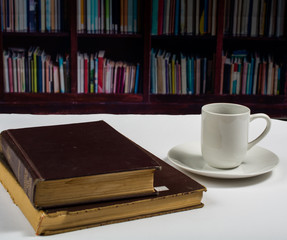 Books and cup of coffee in front of a shelf of books