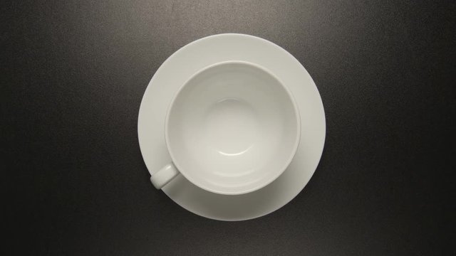 TOP VIEW: White coffee cup is rotating on black background (stop motion)