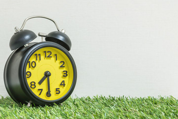 Closeup black and yellow alarm clock for decorate show half past seven or 7:30 a.m. on green...