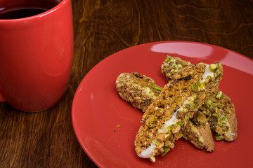 Homemade biscotti on a red plate, with a red coffee cup on a wood table
