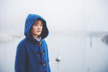 Outdoor portrait of little 9-10 year old little girl on a very foggy day, wearing dark blue coat with hood
