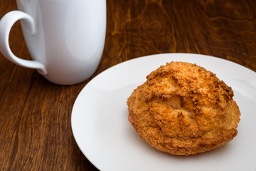 Homemade macaroon on a white plate, with a white coffee cup on a wood table 
