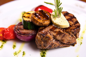 thick steak with rosemary and fried vegetables cheese on white plate. close up