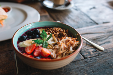 The bowl with smoothie, muesli, fruits and berries on the wooden table