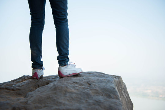 woman legs on mountain peak rock with sunlight