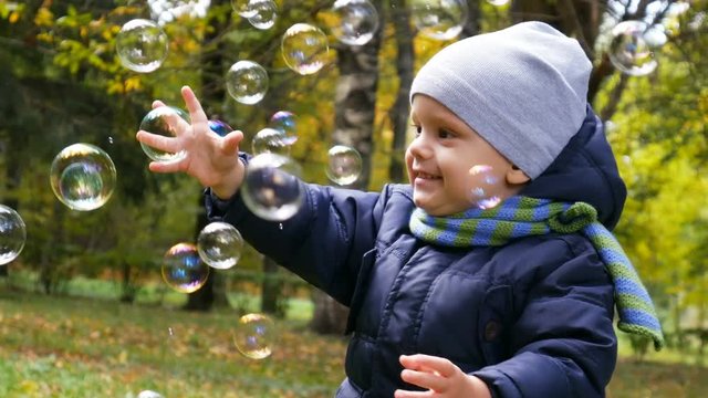 Two years old baby boy playing in park with soap bubbles.