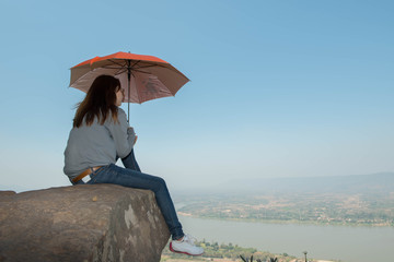 young woman holding umbrella on a cliff rock  with sunlight