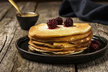 Pile of hot homemade yeast pancakes on a wooden background. Family breakfast. Close-up. Selective focus 