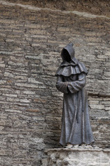 Statue of monk with no face with stone wall on the background.