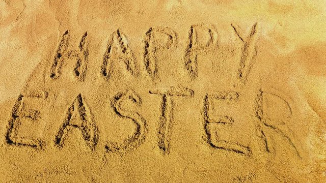 Words Happy Easter appearing letter by letter on the golden sandy beach. Letters are handwritten.      