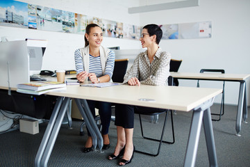 Portrait of two businesswomen, one mature and one young, sitting at desk  in modern office, discussing something  during meeting