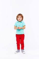 Full body shot of shy little boy dressed in bright colorful clothes standing smiling and twiddling hands against white background