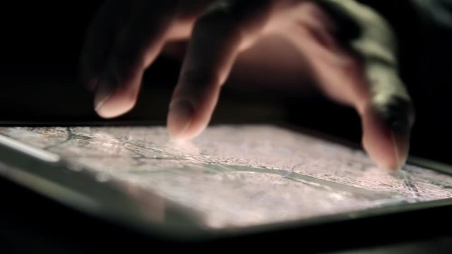 Browsing city map on tablet PC in the dark. Man's hand and screen close-up.