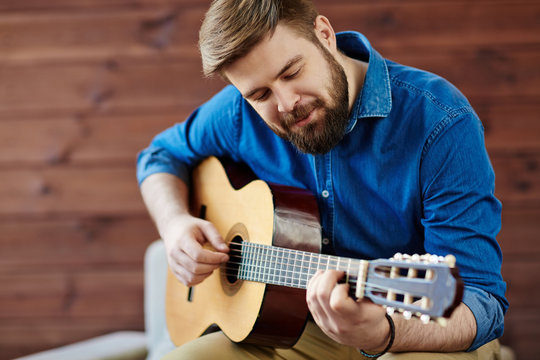 Process of music creation: smiling young man in denim shirt wrapped in composing new melody