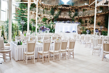 Awesome wedding hall with white chairs and purple flowers on tables.