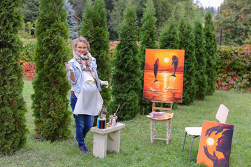 Artist woman holds painting and looks at it, posing at camera an