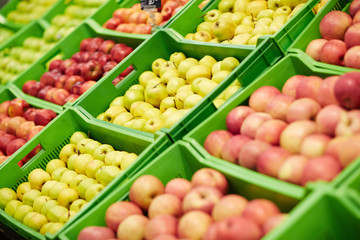 Fresh tasty green, yellow and red apples lying in green plastic boxes in supermarket