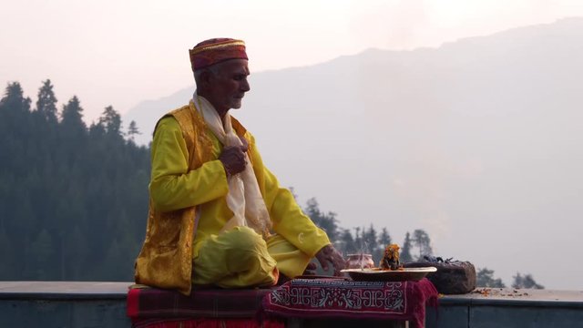 A Hindu old man in yellow national costume offering special spiritual prayer to god in the foothills of the Himalayas, Kullu Valley, India