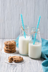 Bottles of milk and chocolate chip cookies on wooden background