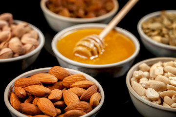 Pistachios, almonds, peanuts, pumpkin seeds, raisins and honey in ceramic plates.