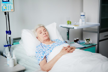 Senior woman asleep on bed after getting her treatment in geriayric hospital