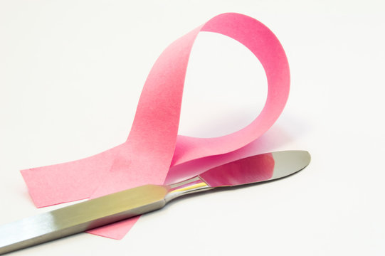 Concept surgery treatment or plastic of breast. Pink ribbon as symbol of breast pathology, lies next to surgical scalpel. Photo for surgery operations such as reconstruction, reduction, uplift ets