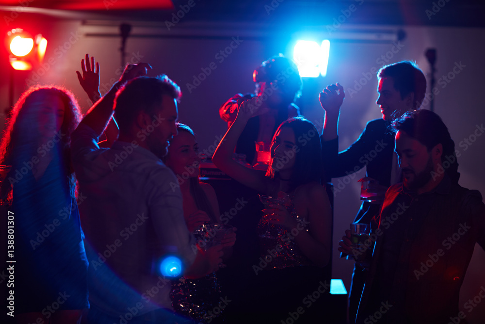 Wall mural young stylish girls and guys enjoying disco party, dancing and drinking while famous dj mixing music