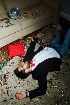Intoxicated Bearded Man With Bow Tie Having Nap On Carpet Covered With Confetti After Wild House Party