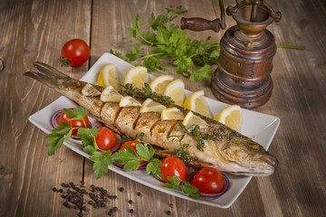 healthy food: two fried sea bass fish served with tomatoes and vegetables on big wooden board over table