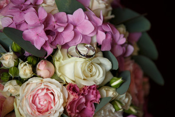 Wedding rings on colorful bridal bouquet of fresh roses and hydrangea