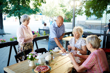Group of elegant-looking senior people relaxing in summer cafe and playing cards with each other