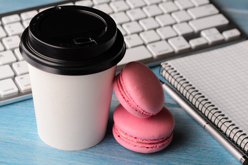 Working on the go. White modern keyboard with coffee cup, candies and notepad on blue wooden table at sunny weather