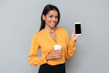 Naklejka premium Business woman holding coffee cup and showing blank smartphone screen