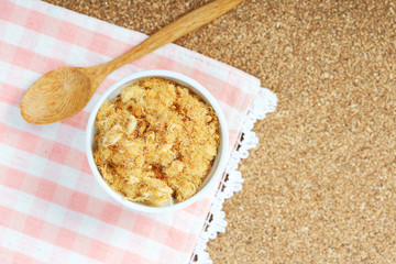 dried pork floss in white cup with wooden spoon on corkboard background.