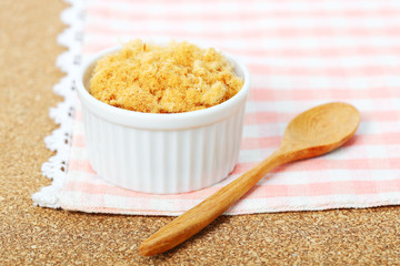 dried pork floss in white cup with wooden spoon on corkboard background.