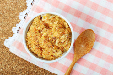 dried pork floss in white cup with wooden spoon on corkboard background.