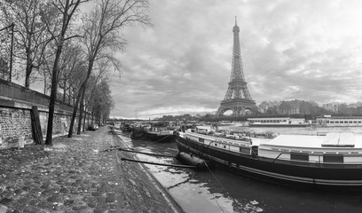 Obraz premium Beautiful panoramic view of the Eiffel Tower and Jena bridge from the river Seine embankment. Dramatic cloudscape. Traditional citycape in backlit morning sunbeam. BW photography. Paris, France.