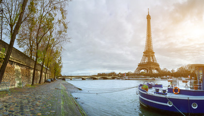 Beautiful panoramic view of the Eiffel Tower and Jena bridge from the river Seine embankment. Dramatic cloudscape. Traditional citycape in backlit morning sunbeam. Paris, France.