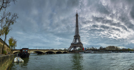 Fototapeta na wymiar Panoramic view of the Eiffel Tower and Jena bridge from the river Seine embankment. Dramatic cloudscape. Paris, France.