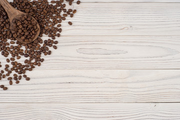 Coffee beans in a wooden spoon on a white wooden table.