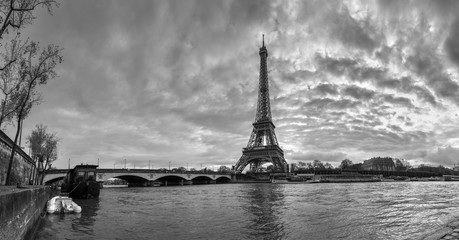 Beautiful panoramic view of the Eiffel Tower and Jena bridge from the river Seine embankment. Dramatic cloudscape. BW photography. Paris, France.