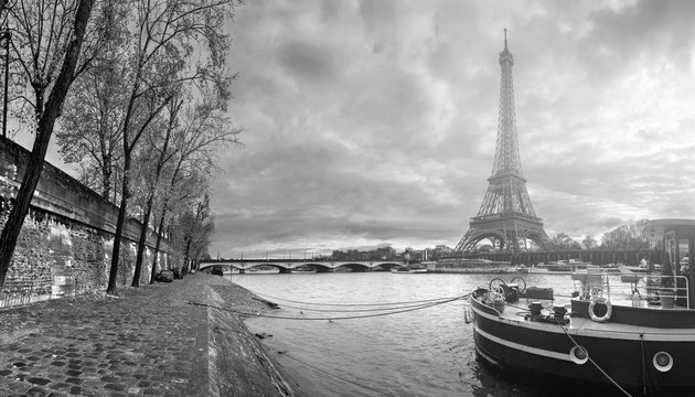 Beautiful panoramic view of the Eiffel Tower and Jena bridge from the river Seine embankment. Dramatic cloudscape. Traditional citycape in backlit morning sunbeam. BW photography. Paris, France.