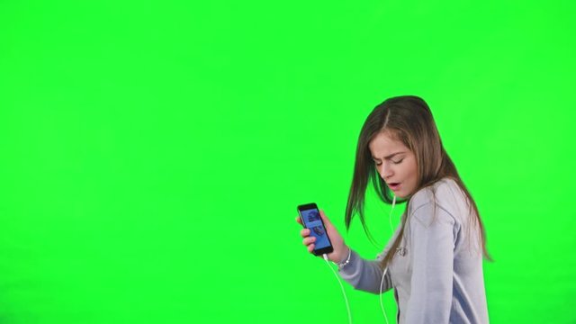 Happy Young Woman Sing And Dancing, Listening To Music On Smartphone, A Woman Is Dancing On His Own Against A Green Background. Easy To Key Out And Add Your Own Background.