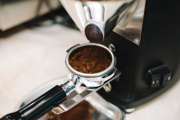 freshly ground coffee beans in a portafilter by the coffee grinder
