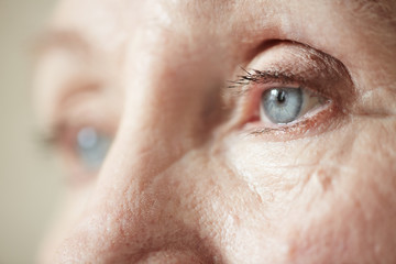Sad blue-grey eyes of elderly woman looking to the side, extreme close-up shot - obrazy, fototapety, plakaty