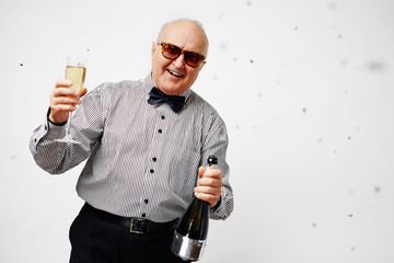 Portrait of stylish elderly man in striped shirt with bow tie holding a glass of champagne, making...