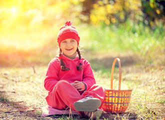 Laughing happy little girl with a basket sitting in the forest on picnic