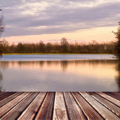 Naklejka na ściany i meble Wooden deck floor on sunset lake with trees and sky